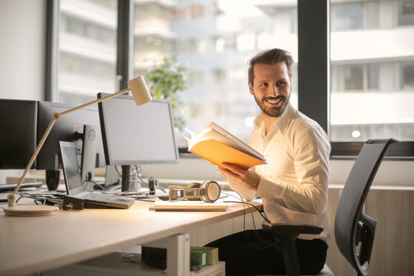 homem sorri enquanto segura um livro aberto em seu escritório