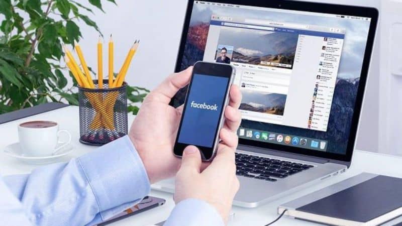 laptop com facebook e mãos no celular com lápis e caderno do facebook